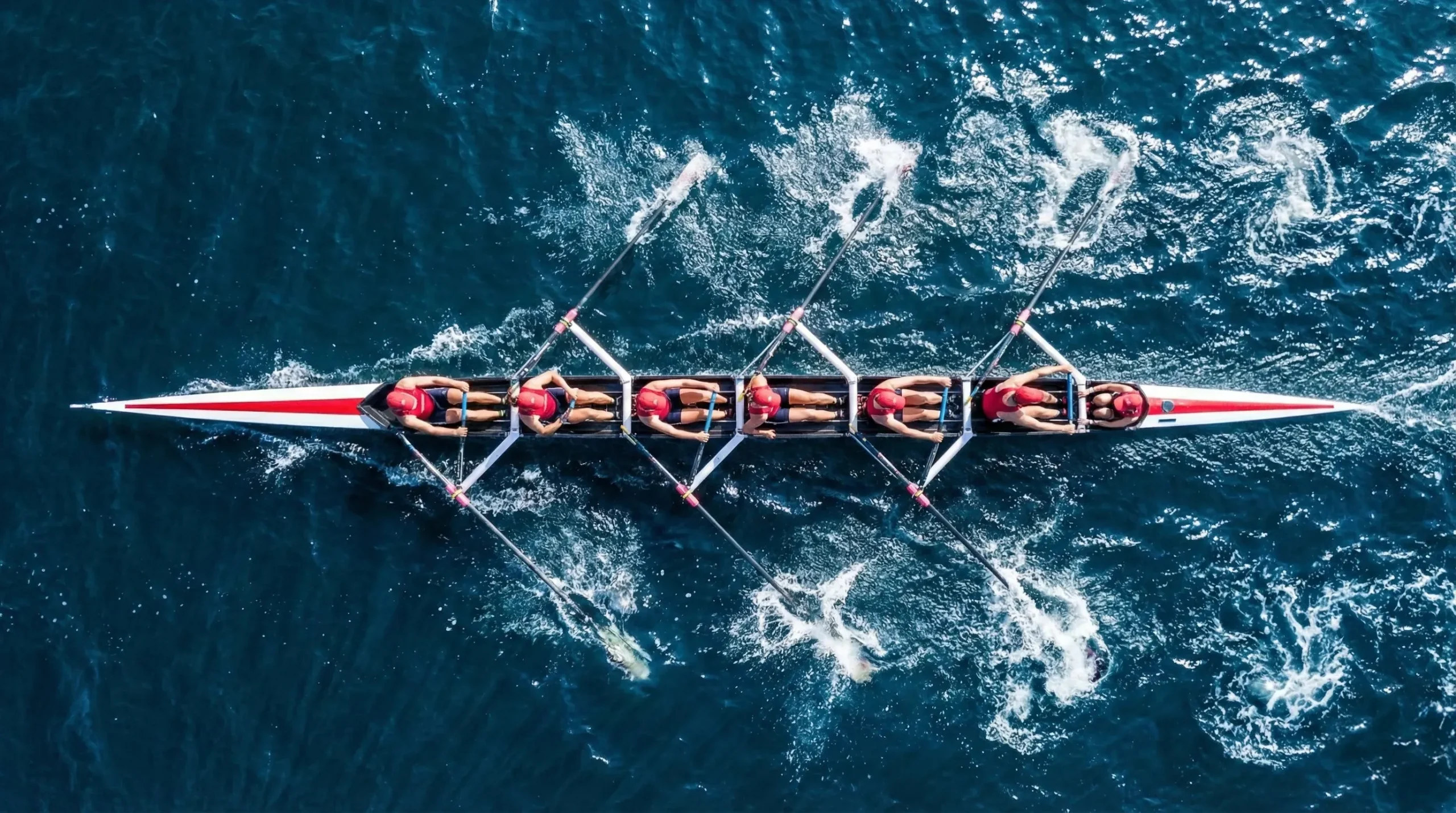 Aerial view of a rowing team paddling together on dark blue water