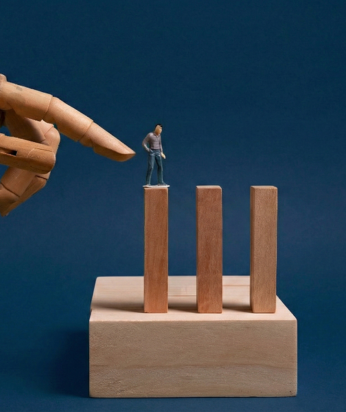 Wooden hand pointing at a miniature figurine standing on top of the tallest wooden block