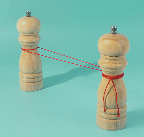 Two wooden pepper mills connected by a red string on a teal background
