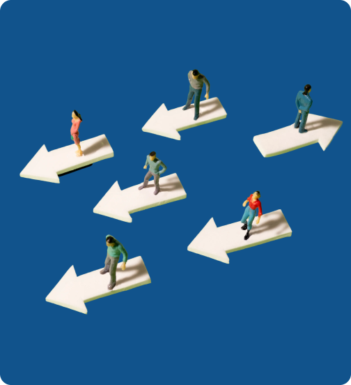 Miniature people figurines standing on white arrows pointing in different directions on a blue background